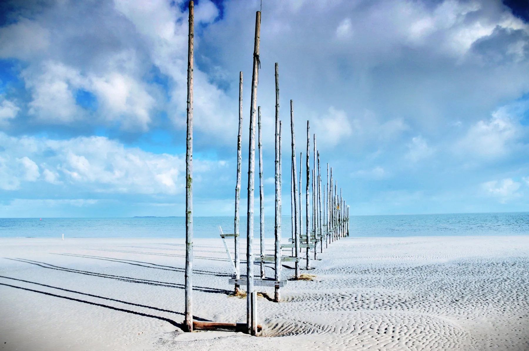 Breed Texels strand met houten palen en wolkenlucht